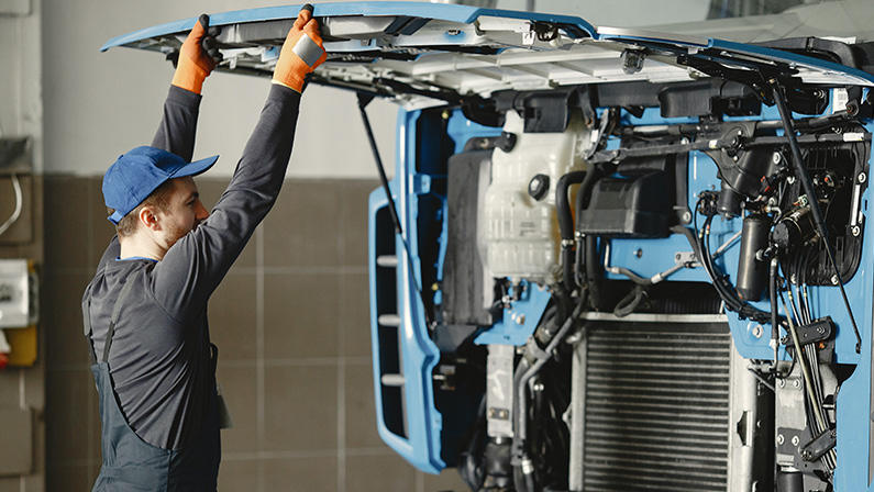 Man in Working Clothes Looking Under the Hood of Blue Truck