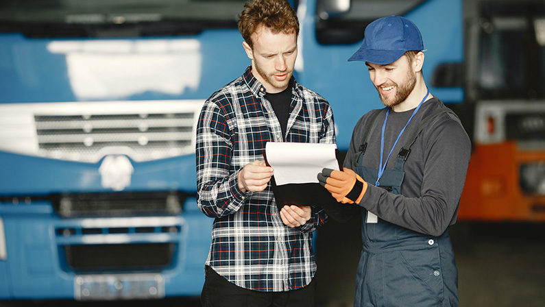 Man in Plaid Shirt and Man in Working Clothes Looking at the Papers