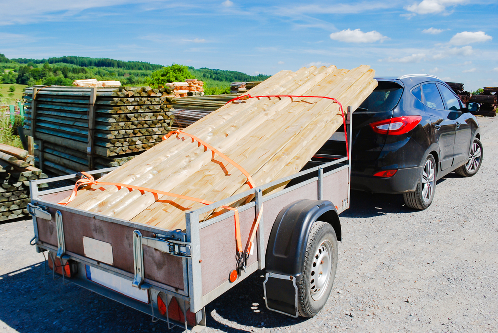Outdoor stacking the logs on utility trailer for transport at sawmill in europe with background green forest