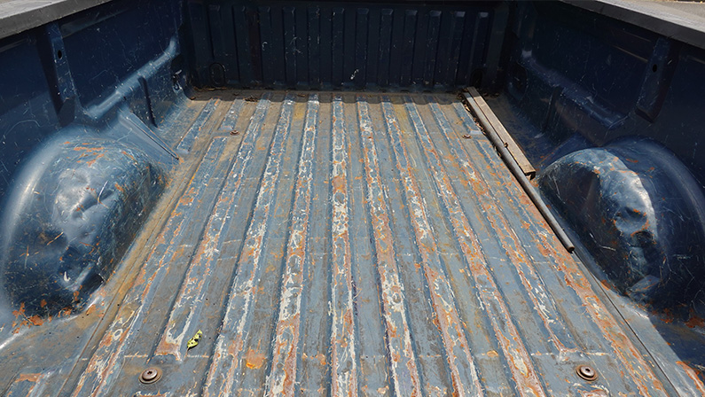 Back of a slightly rusted truck bed looking towards the cab.