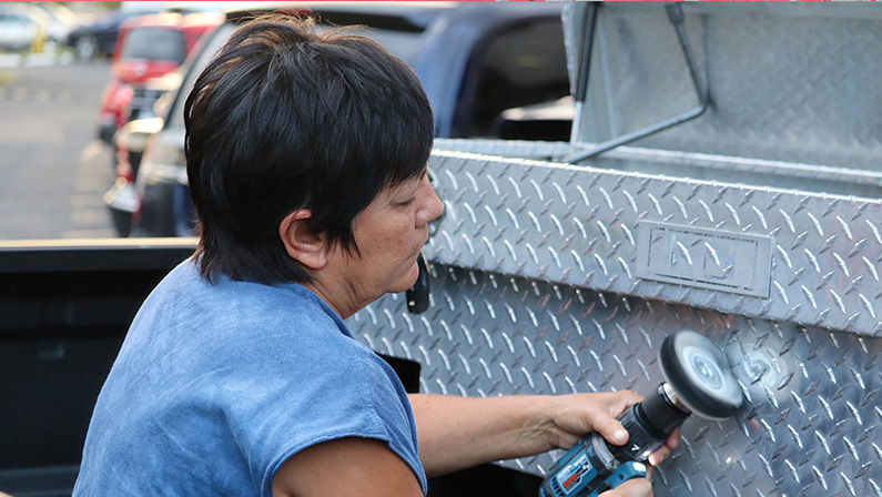 Woman Polishing Aluminum Toolbox with Power Tool While Sitting in Truck Bed