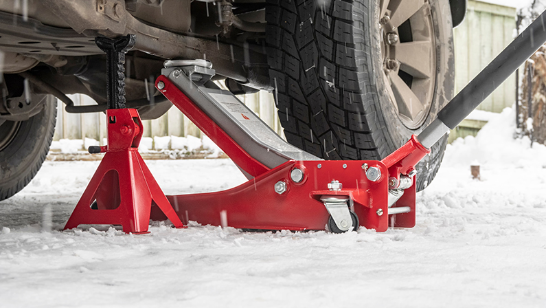 Hydraulic Trolley Jack Car Lift and Jack stand for changing car wheels. Replacing wheel in winter on snowy road in snowfall.